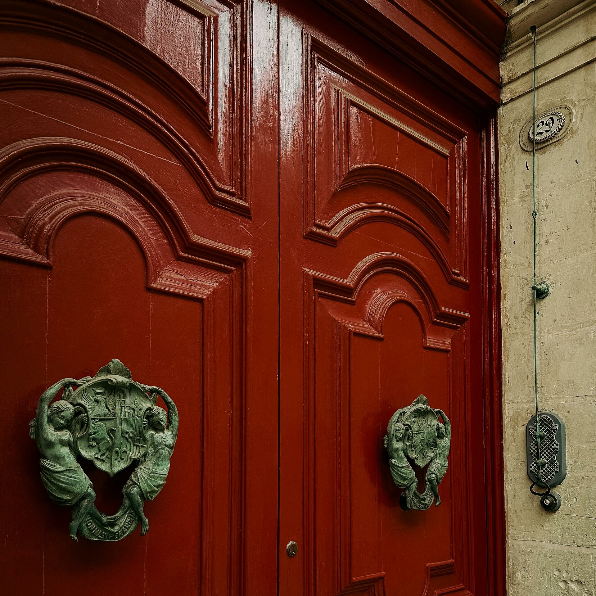 Classic red door with ornate bronze knockers in Malta, showcasing architectural detail and heritage style.